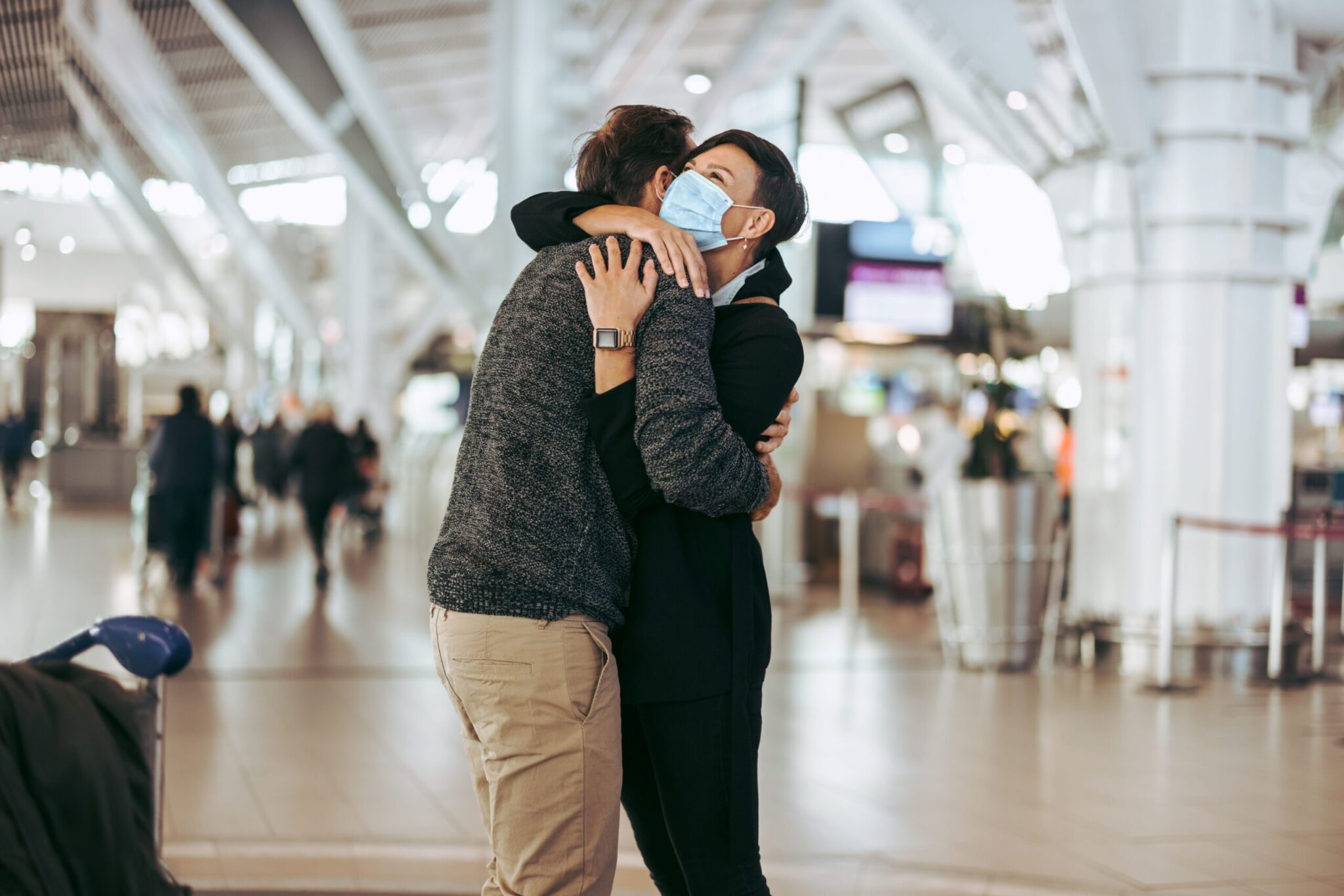 On the cover of the 2021 ACI Annual Report, two people hug in an airport terminal—one in a face mask and dark clothes, the other in a sweater and beige pants—with blurred travelers and modern architecture in the background.