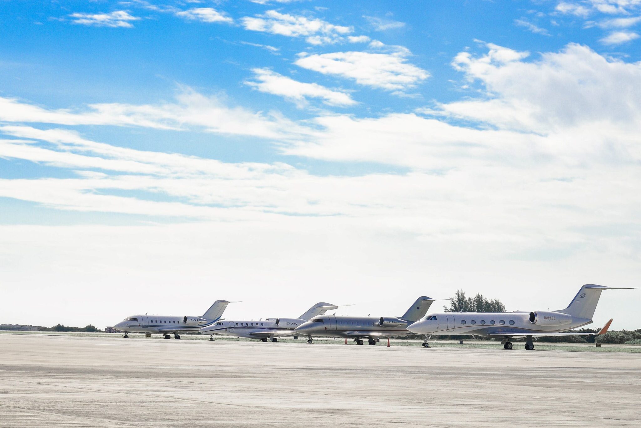 Four private jets lined up on an airport tarmac beneath a partly cloudy sky, featured in the ACI World Airport Slot Policy Forums Proceedings, 2021, with trees in the distant background.