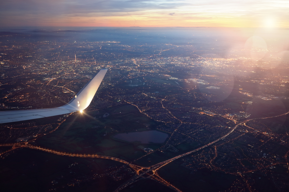 Aerial view from a plane window at sunset, with city lights and an aircraft wing visible, illustrating the scope of Environmental, Social, and Governance (ESG) Management Best Practice.