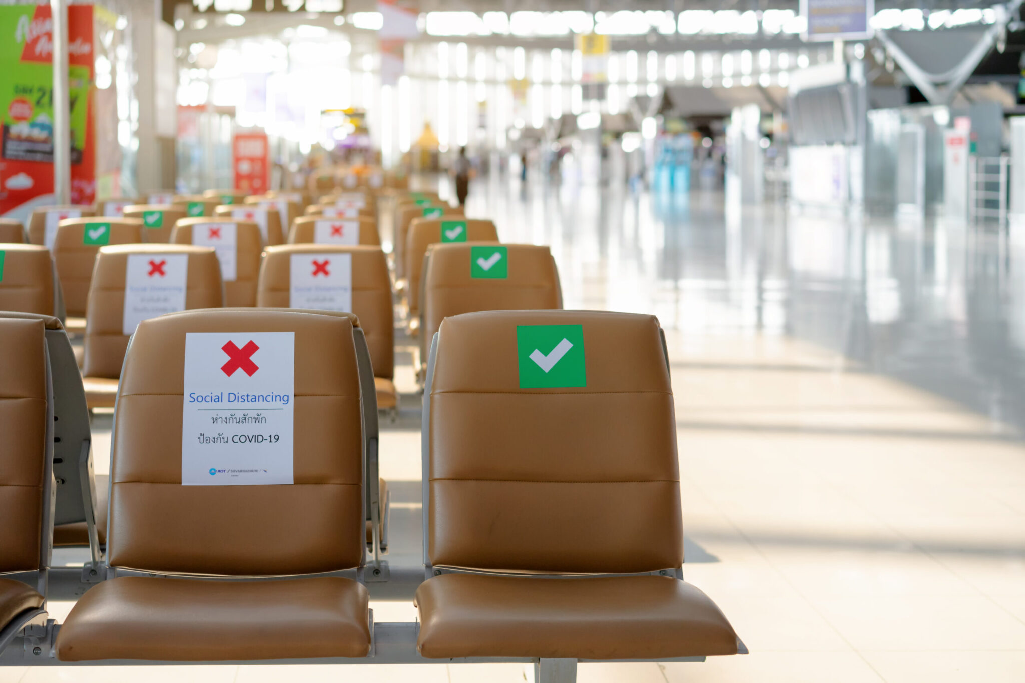 Rows of brown airport seats display red Xs and green checks for social distancing. A sign reads “Social Distancing” with COVID-19 guidance, highlighting new realities of customer experience in the pandemic era. Product: New Realities of Customer Experience.