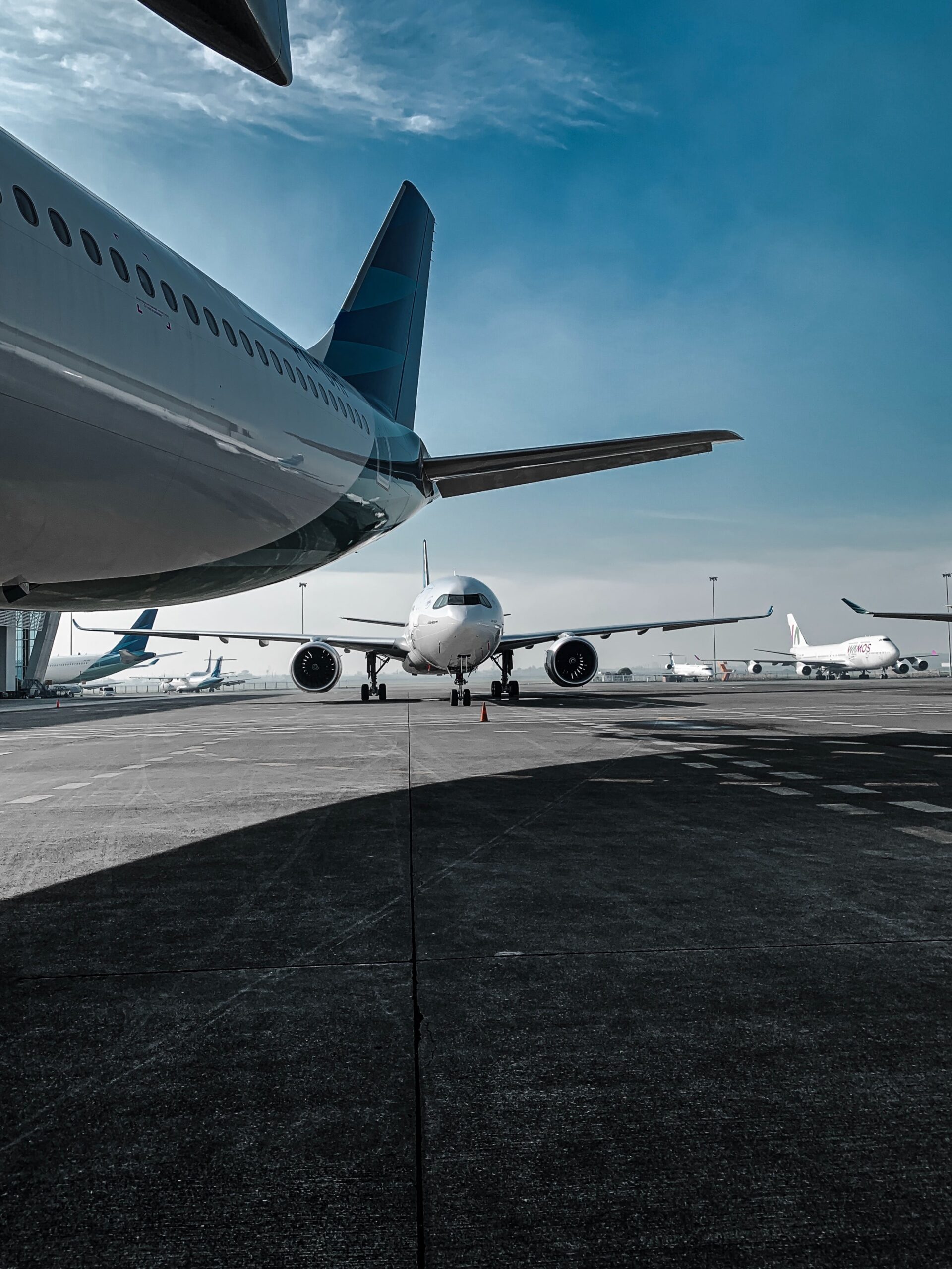 A commercial airplane taxis on an airport runway, with other aircraft nearby, beneath a blue sky—highlighting the need for transparency and consultations as outlined in the Recommended Practices on Setting Airport Charges.
