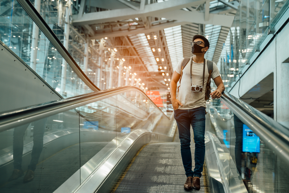 A traveler stands on a moving walkway in a modern airport, exemplifying the journey focus of 