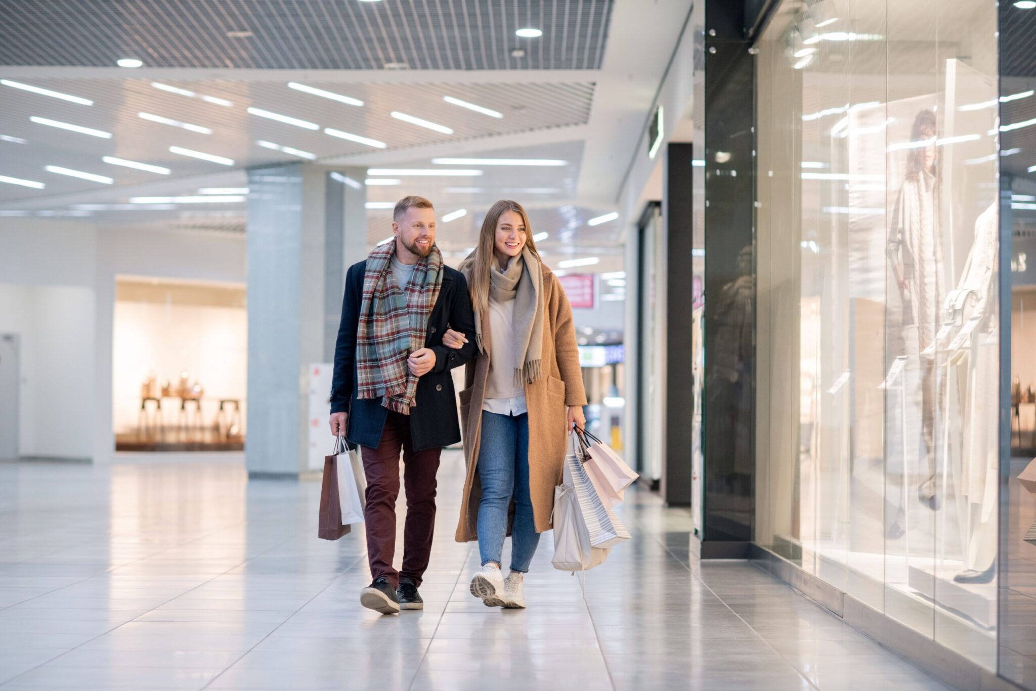 A couple, dressed in winter attire, strolls through a bright, spacious airport retail area—illustrating insights from the 