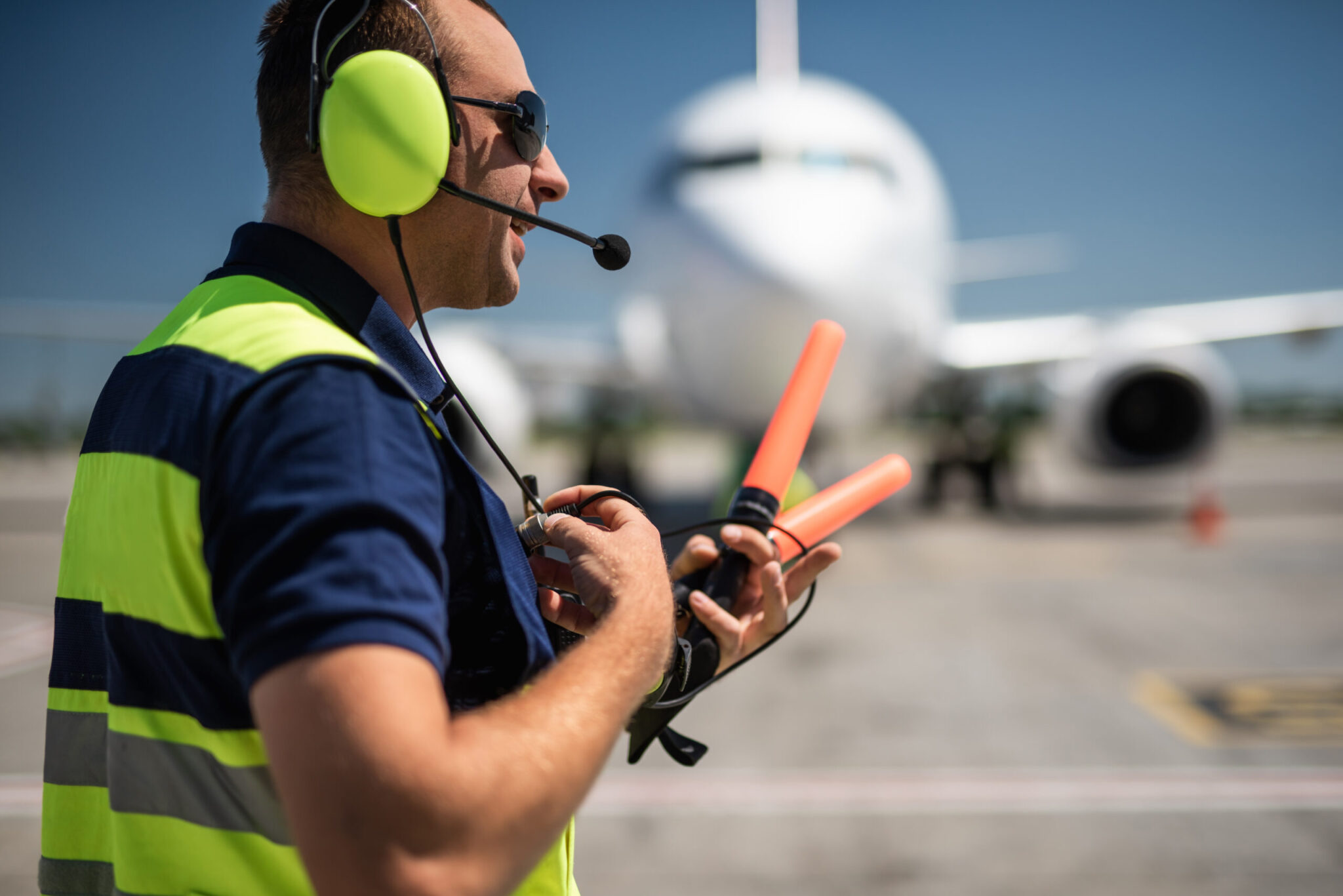 A ground crew worker guides a plane on the tarmac, illustrating the need for stronger collaboration between airports and ground handlers as discussed in 