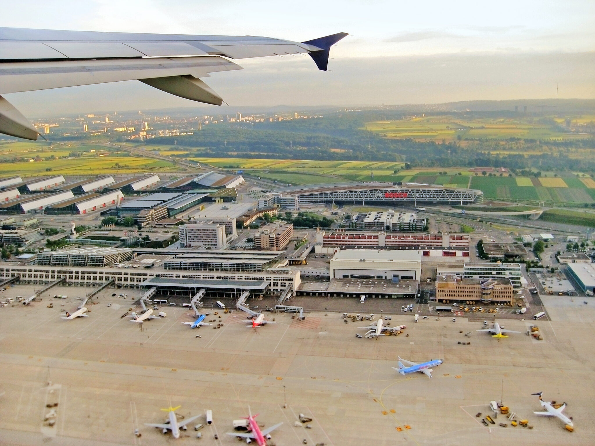 Aerial view from a plane window shows an airport terminal with parked airplanes and a cityscape, featured on the cover of 