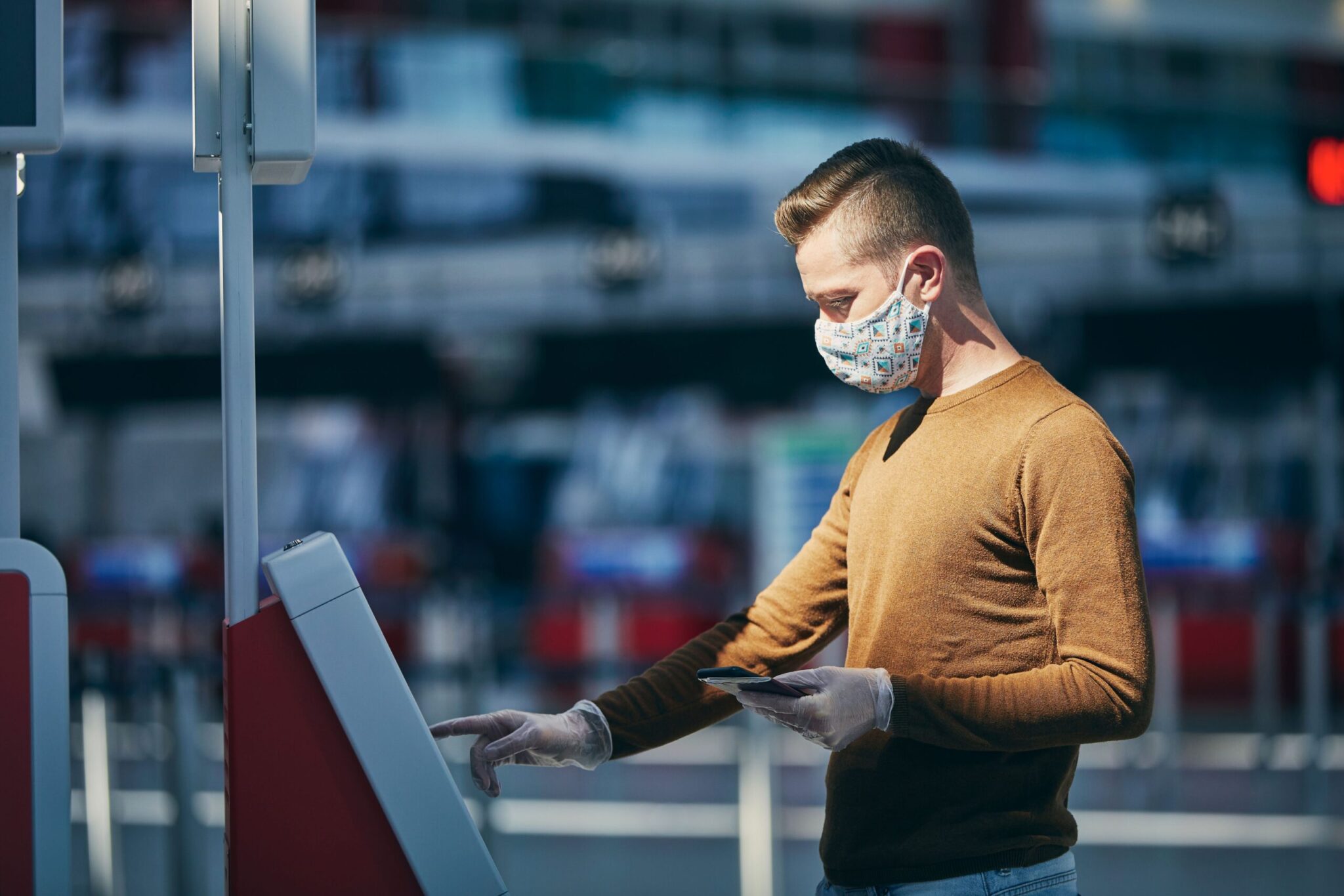 A man uses a touchscreen kiosk while holding a phone, representing the need for tailoring airport charges and economic regulation to support airports' economic recovery in public spaces like airports.