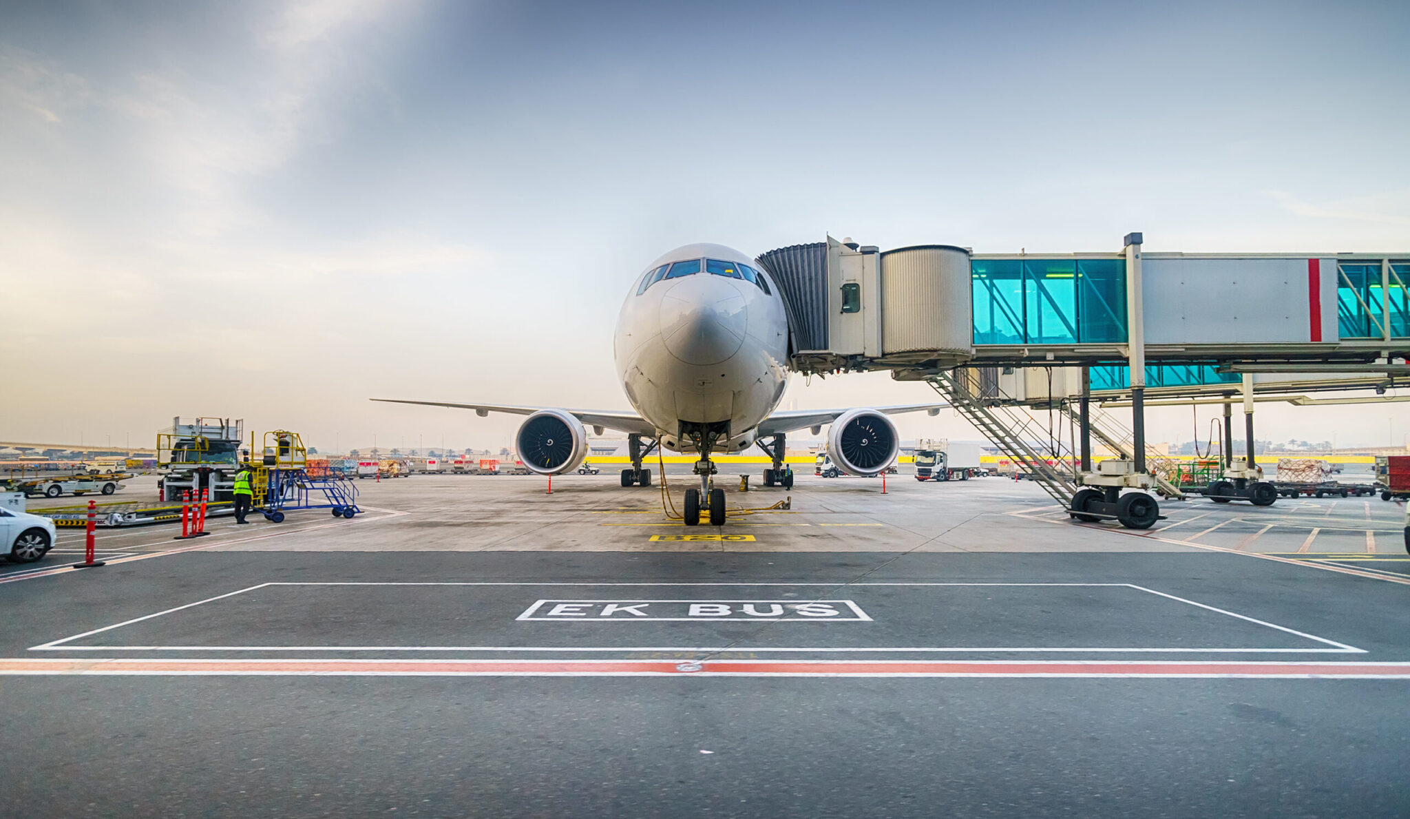 An airport scene shows a large commercial jet at a gate with ground crew, vehicles, and marked signage such as 