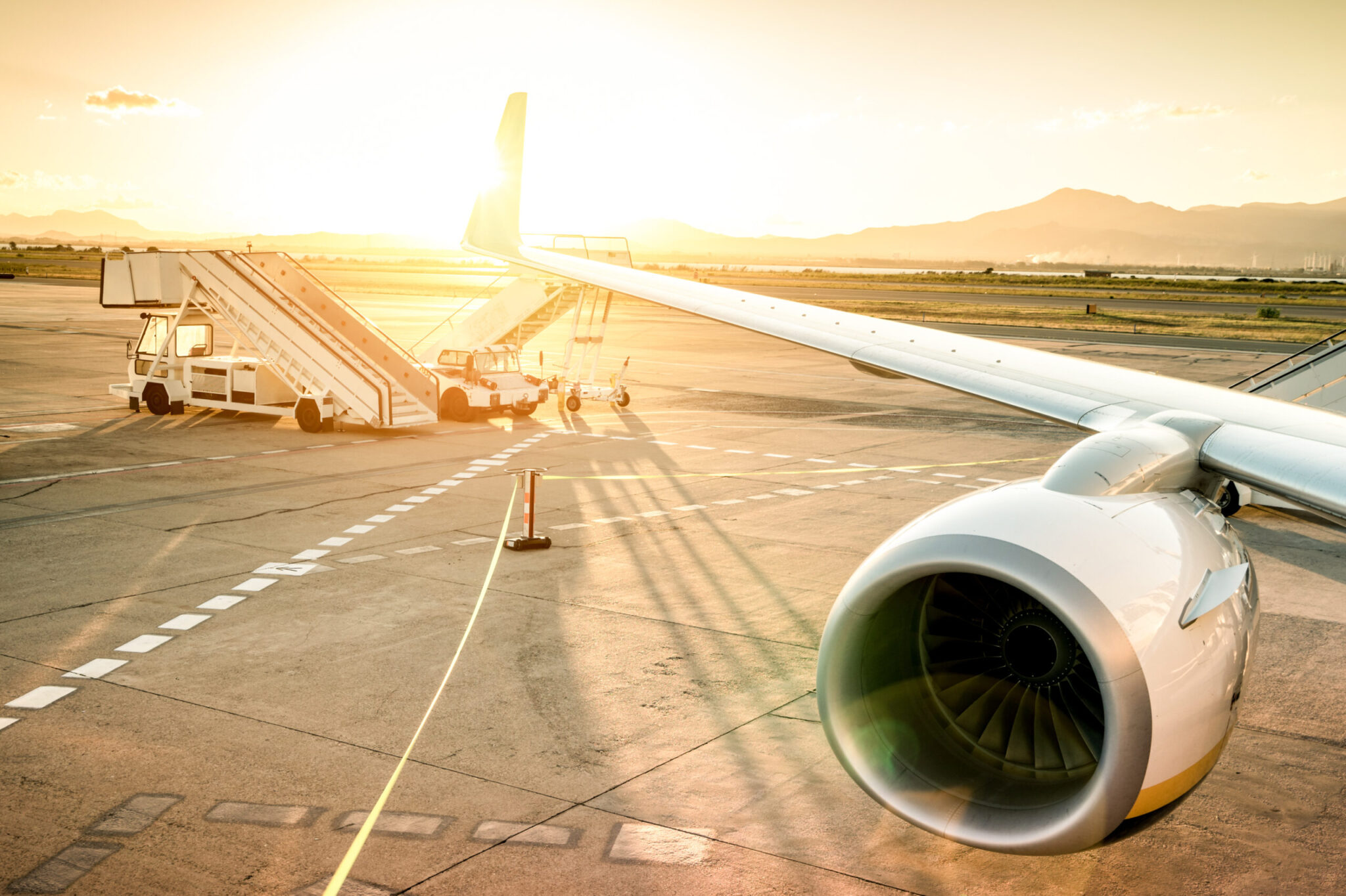 A close-up of an airplane wing and engine on the tarmac at sunset highlights 