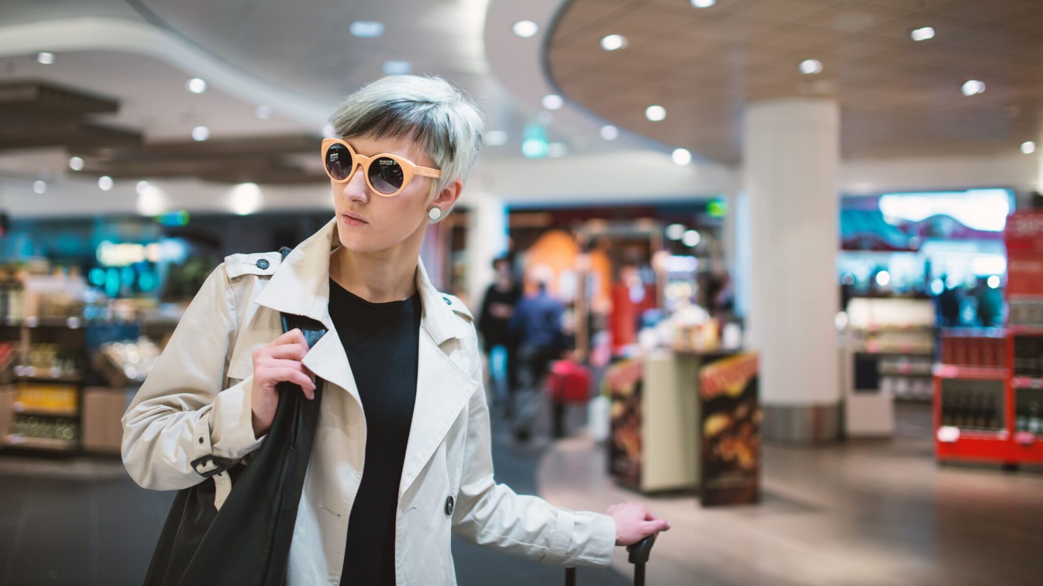 A person stands in an airport retail area with a black bag and suitcase, highlighting the setting discussed in the white paper 