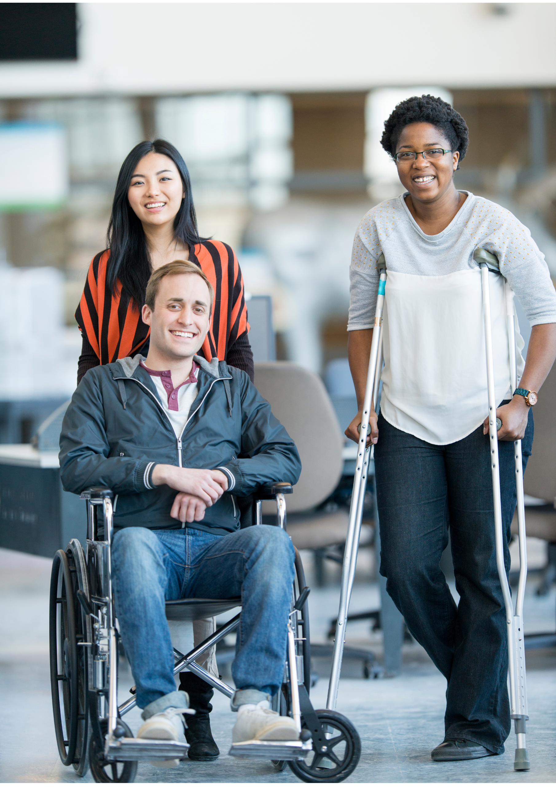 Three people indoors—a smiling man in a wheelchair, a woman behind him, and another woman using crutches—all look confident and happy. Scene for 