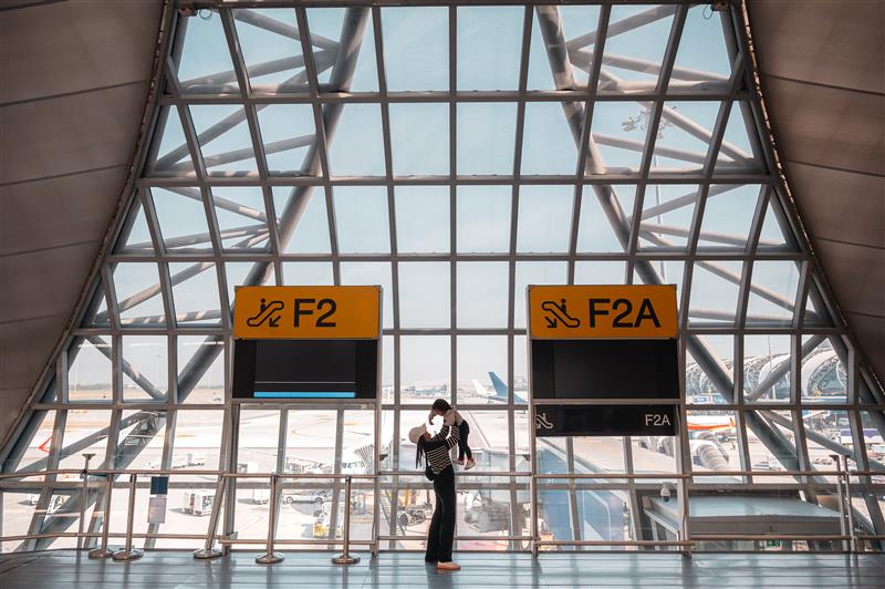 A couple embraces near gates F2 and F2A with planes visible outside, capturing a moment of travel in the setting featured in the Annual World Airport Traffic Report, 2025.